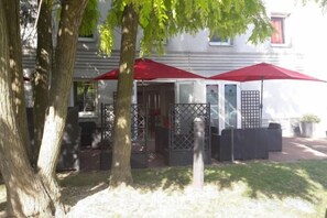 Un patio con mobiliario exterior, una sombrilla roja y un edificio al fondo.