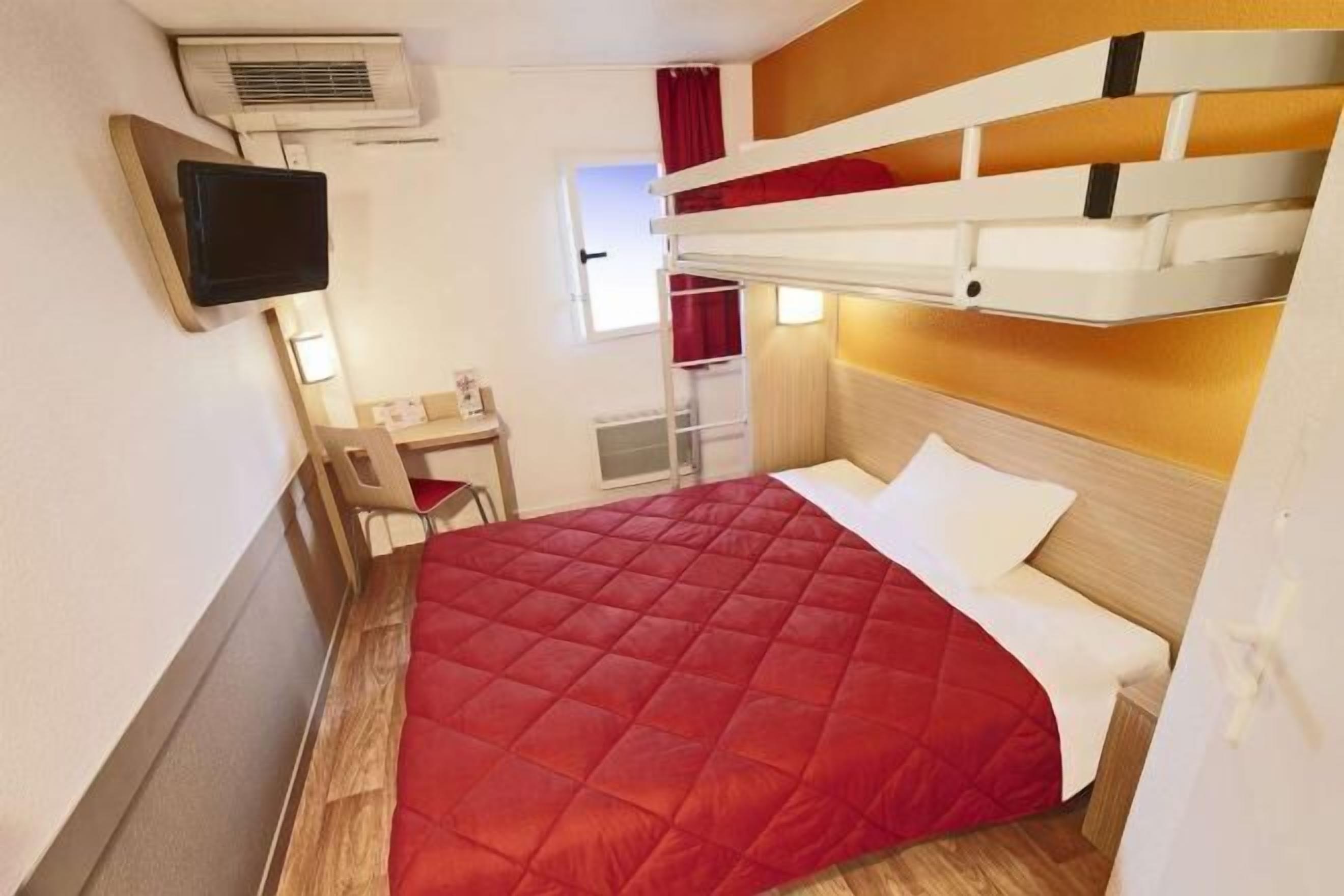Una habitación de hotel compacta con literas, un escritorio, una silla y un televisor.