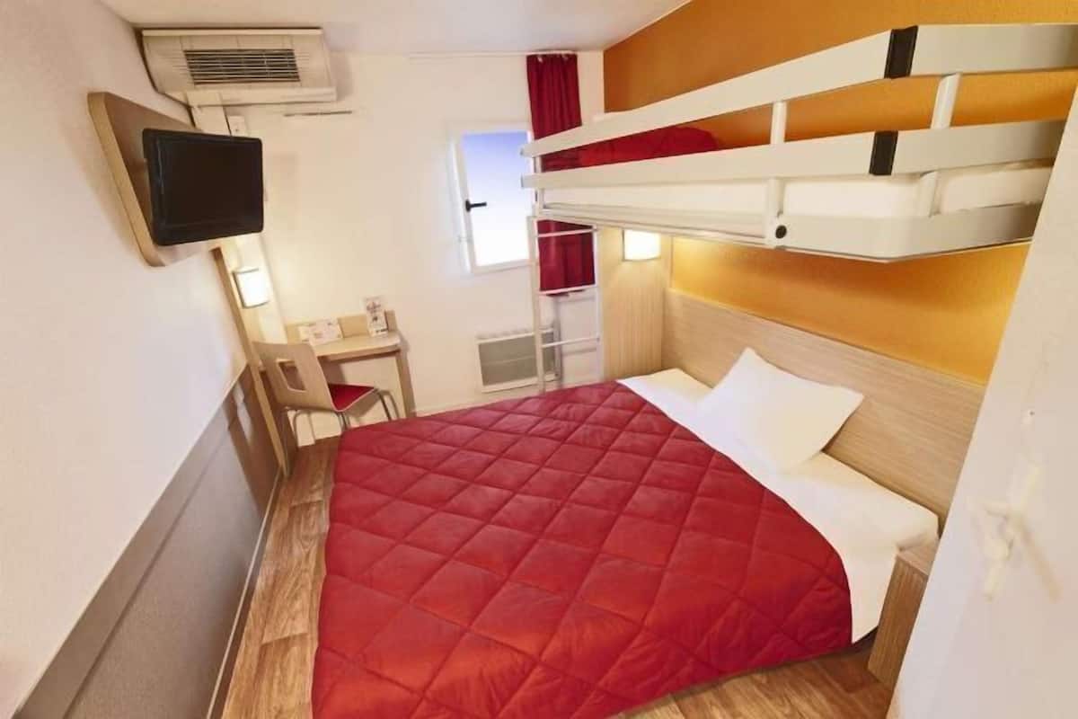 Ein kleines Hotelzimmer mit Stockbetten, einem Schreibtisch, einem Stuhl und einem Fernseher.