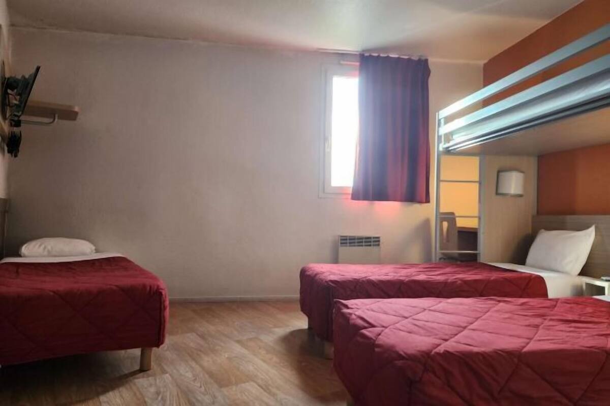Ein Zimmer mit zwei Betten, einem Fenster mit Vorhängen, einem Nachttisch und einer Lampe.