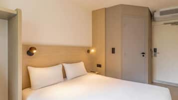 A hotel room with a bed, a nightstand, a wall-mounted light, and a door.