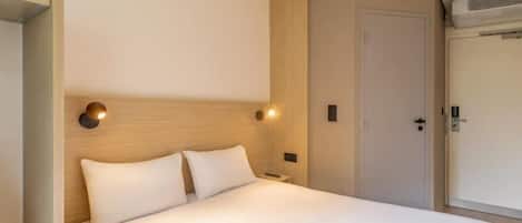 Una habitación de hotel con una cama, una mesita de noche, una lámpara de pared y una puerta.