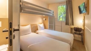 Une chambre avec deux lits, un bureau, une chaise, une télévision et une fenêtre avec des rideaux.