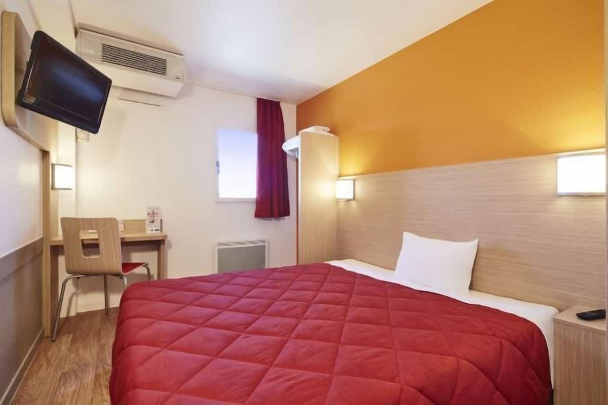 Ein Hotelzimmer mit Bett, Schreibtisch, Sessel, Fernseher und einer Wand-Klimaanlage.