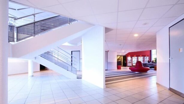 Un hall d’entrée spacieux avec un escalier, un coin salon rouge et un sol carrelé.