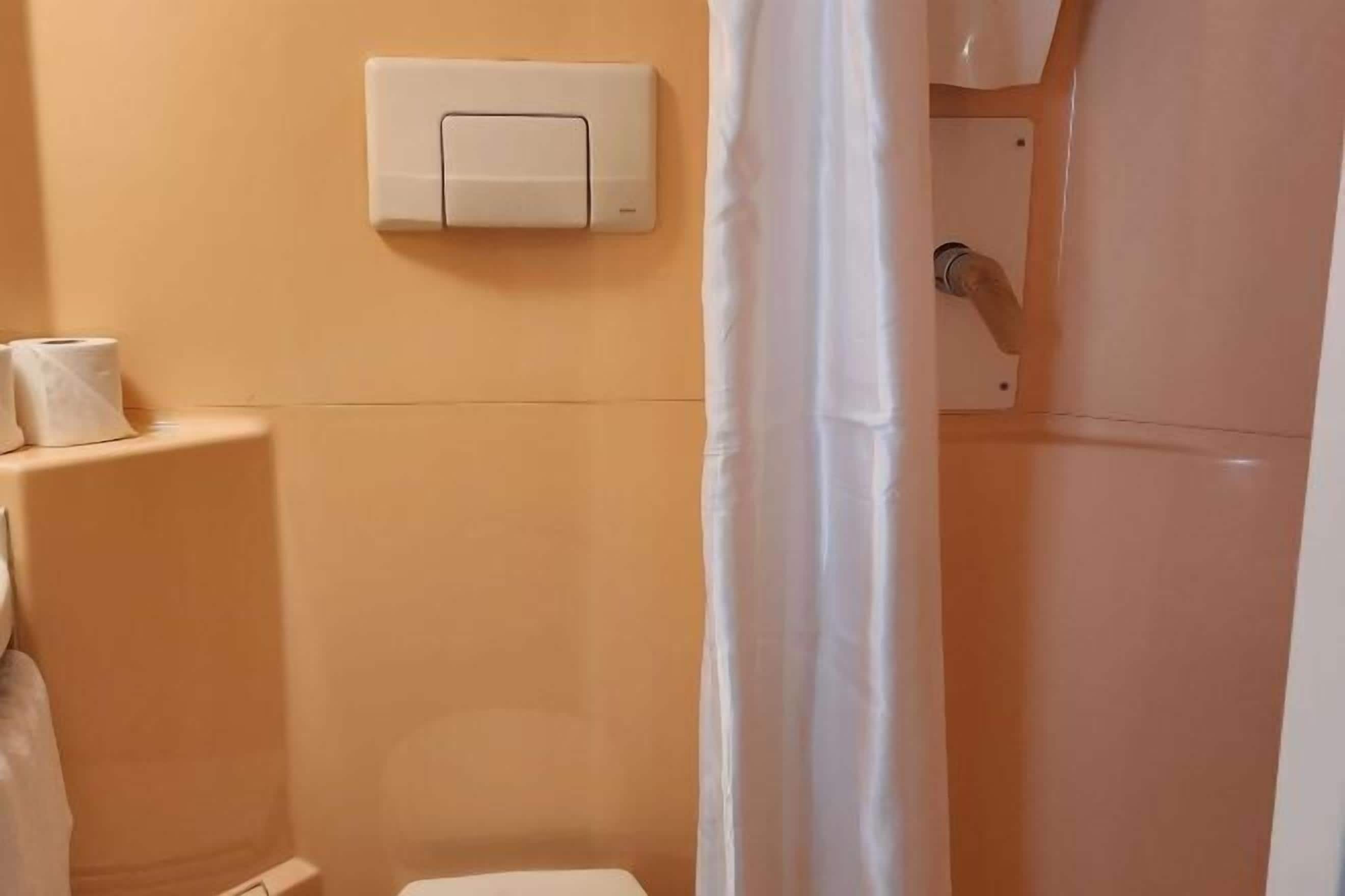 Un baño con inodoro, un accionador de descarga en la pared y una cortina de ducha.