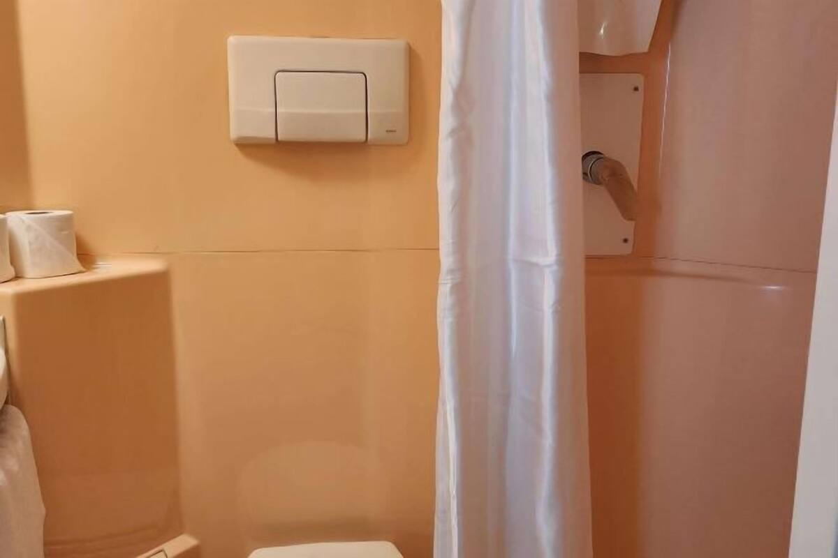 Un baño con inodoro, un accionador de descarga en la pared y una cortina de ducha.
