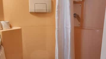A bathroom with a toilet, a wall-mounted flush handle, and a shower curtain.