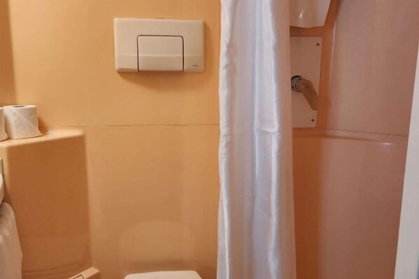 Un baño con inodoro, un accionador de descarga en la pared y una cortina de ducha.
