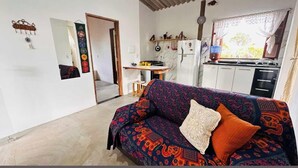 Un salon chaleureux avec un canapé à motifs, une petite table et un coin cuisine équipé d’un réfrigérateur et d’une cuisinière.