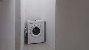 A compact, white laundry room with a built-in washer and dryer, a small vent, and a tiled floor.