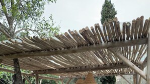 A covered outdoor seating area with a wooden pergola, a cushioned sofa, a wooden coffee table, and a wicker basket. - Charming sheepfold with private heated pool between sea and mountains (Sotta)