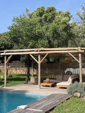 A wooden pergola with a cushioned seating area and a pool. - Charming sheepfold with private heated pool between sea and mountains (Sotta)