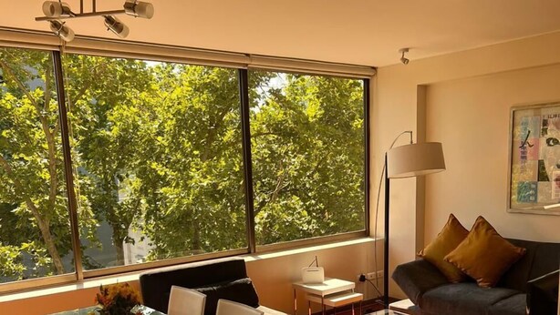 Un saló modern amb una taula de dinar de vidre, un sofà i una finestra gran amb vista a arbres.