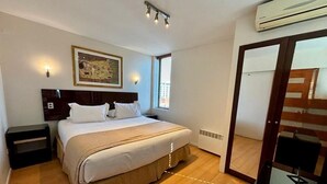 Una habitació amb un llit, taules de nit, aire condicionat fixat a la paret i una finestra amb persianes.