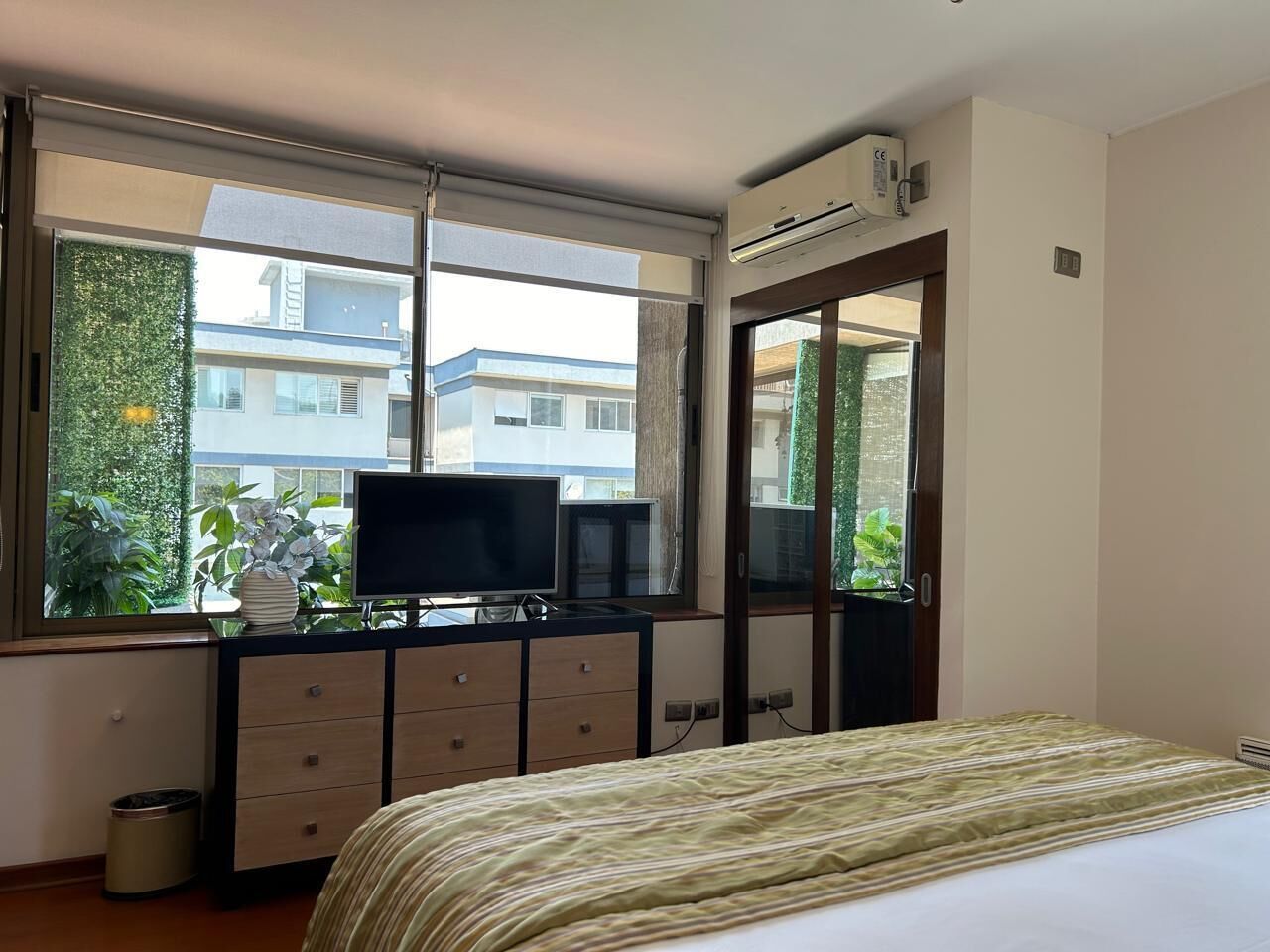 Hotelkamer met een bed, een televisie op een dressoir, een raam met uitzicht op gebouwen en een airconditioning.