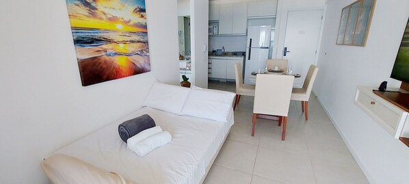 A small hotel room with a bed, a dining table with chairs, a kitchen area, and a painting of a sunset. - COBAR0125 - Edifício 535 Barra (Salvador)