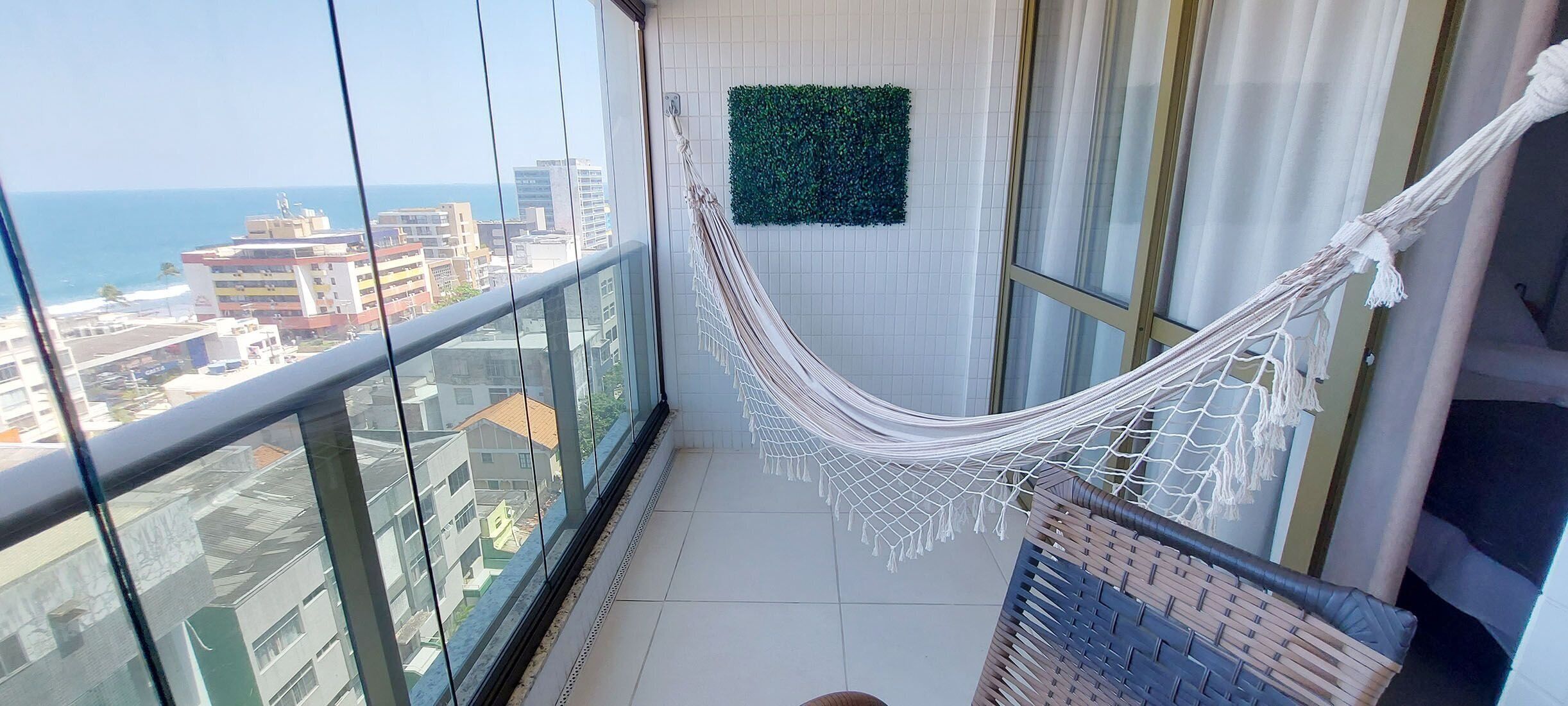 A balcony with a hammock, a view of the city, and a green wall decoration.