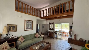A spacious living area with a green sofa, a coffee table, and a wooden staircase. - Charming House Galé (Grândola)