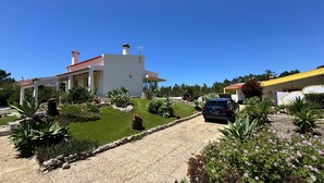 A modern house with a white exterior and red roof, surrounded by a well-maintained garden with various plants and a gravel driveway. - Charming House Galé (Grândola)