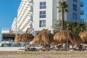 A beachside hotel with thatched umbrellas, sun loungers, and a tall building with balconies.