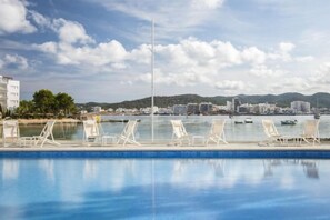 A swimming pool with lounge chairs, a clear sky, and a distant view of buildings and hills. - Innside by Meliá Ibiza (Ibiza)