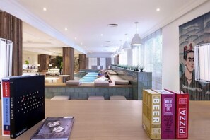Una moderna hall d'albergo con piscina, zona salotto e libri su un tavolo.