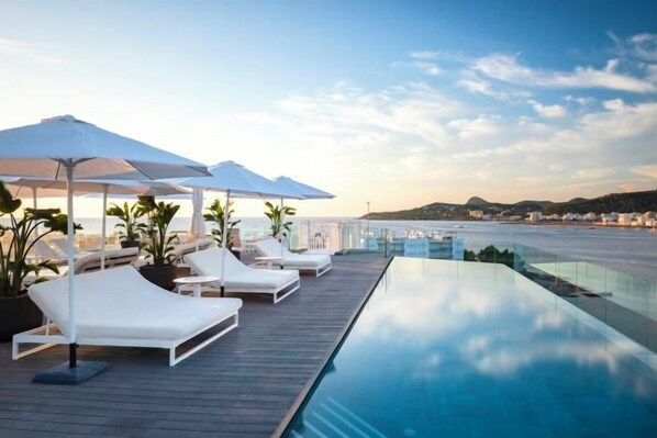 An infinity pool with lounge chairs and umbrellas, overlooking a coastal area.