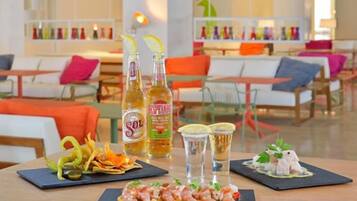 Una mesa de comedor con una variedad de platos, incluyendo camarones y un postre, en un moderno entorno hotelero con sillas color naranja y un interior luminoso.