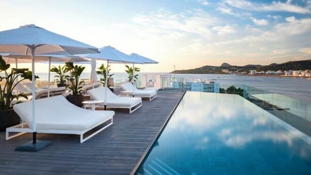 A rooftop infinity pool with white lounge chairs and umbrellas, overlooking a coastal cityscape. - Innside by Meliá Ibiza (Ibiza)