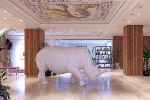 Una estatua grande de rinoceronte blanco en un vestíbulo con un panel de madera y un techo con diseños intrincados.