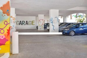 Un parcheggio multipiano con diverse auto parcheggiate, pilastri bianchi e un muro colorato con motivi astratti.