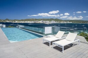 Una piscina en la azotea con agua cristalina, con vistas a un puerto deportivo con barcos y un horizonte costero.