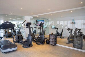 A gym with various cardio machines, a mirrored wall, and a large window. - Innside by Meliá Ibiza (Ibiza)