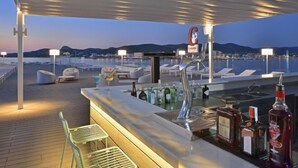 A bar area with lounge seating, a bar counter with bottles, and a view of the water and mountains in the background. - Innside by Meliá Ibiza (Ibiza)