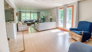 Un vaste espace de vie comprenant un canapé, un fauteuil bleu et un meuble de rangement blanc pour les appareils multimédias.