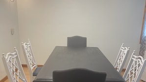 Un coin repas comprenant une table rectangulaire, quatre chaises blanches à dossier ajouré et un lustre moderne.