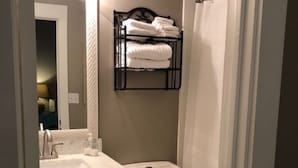 Une petite salle de bain avec un lavabo blanc, des toilettes et une petite étagère au-dessus des toilettes où sont rangées les serviettes.