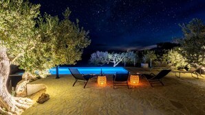 An outdoor pool area with lounge chairs and decorative lighting, surrounded by trees and a night sky. - Holiday home House of the Sun - Three Bedroom Holiday Home with Pool (Sutivan)