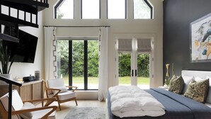 A bedroom with a bed, a desk, and a chair. There are large windows and a view of greenery outside. - Fall in LOVE with The Infinity Stay Collection and enjoy the Magic it offers. (Carriere)
