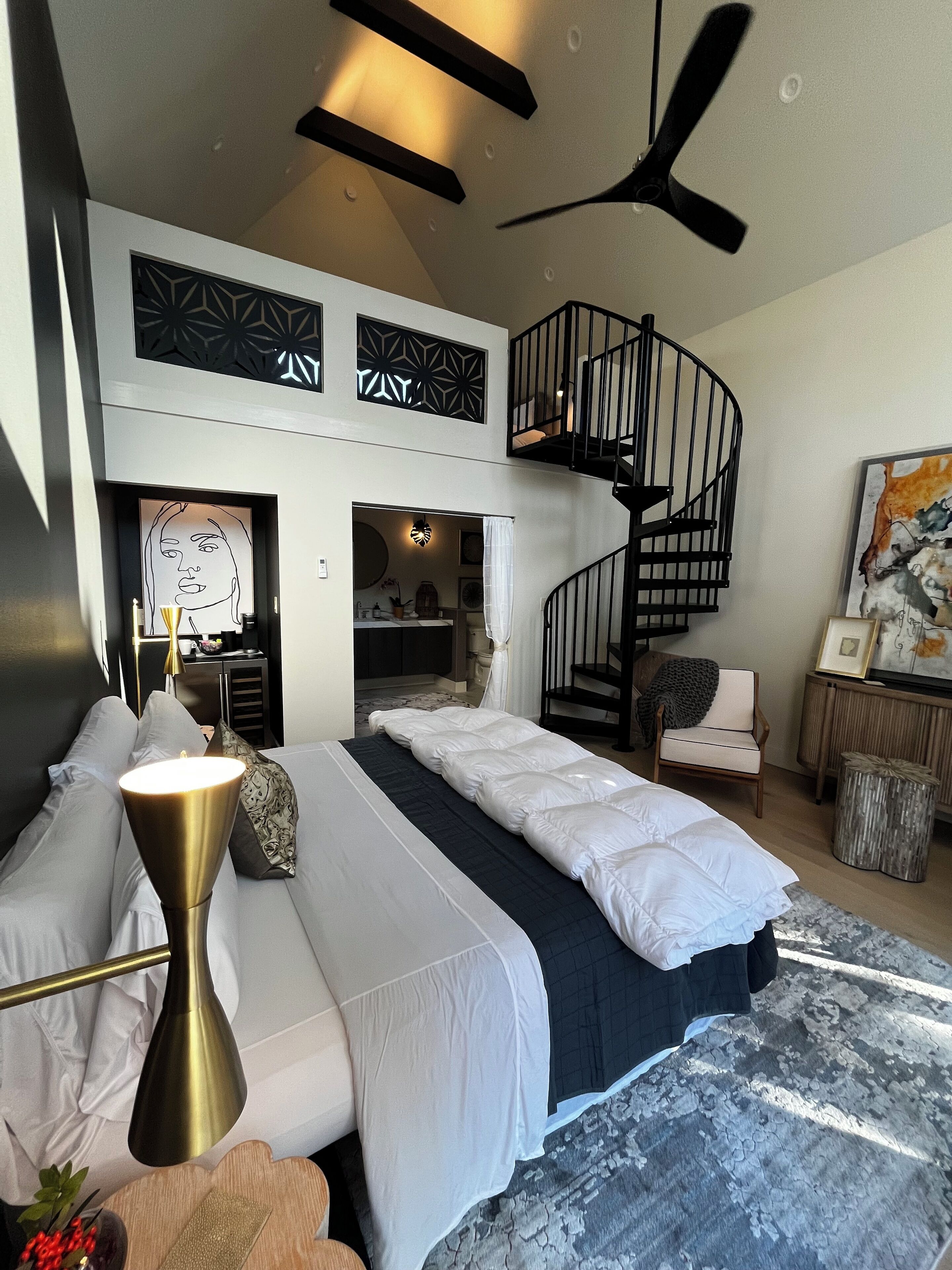 A modern bedroom with a large bed, a spiral staircase, and a view of the bathroom.
