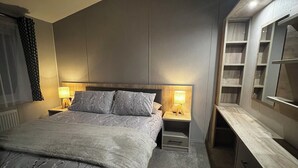 A modern bedroom with a large bed, bedside tables with lamps, a built-in wardrobe, and a slanted ceiling. - Modern, spacious lodge at Hunter's Quay Holiday Park. (Dunoon)
