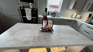 A kitchen with a central island, two wooden stools, a bottle of wine, and a bag of mini chocolate chip shortbread. - Modern, spacious lodge at Hunter's Quay Holiday Park. (Dunoon)