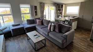 A modern living room with a sectional sofa, a coffee table, and a dining area with a table and chairs. - Modern, spacious lodge at Hunter's Quay Holiday Park. (Dunoon)