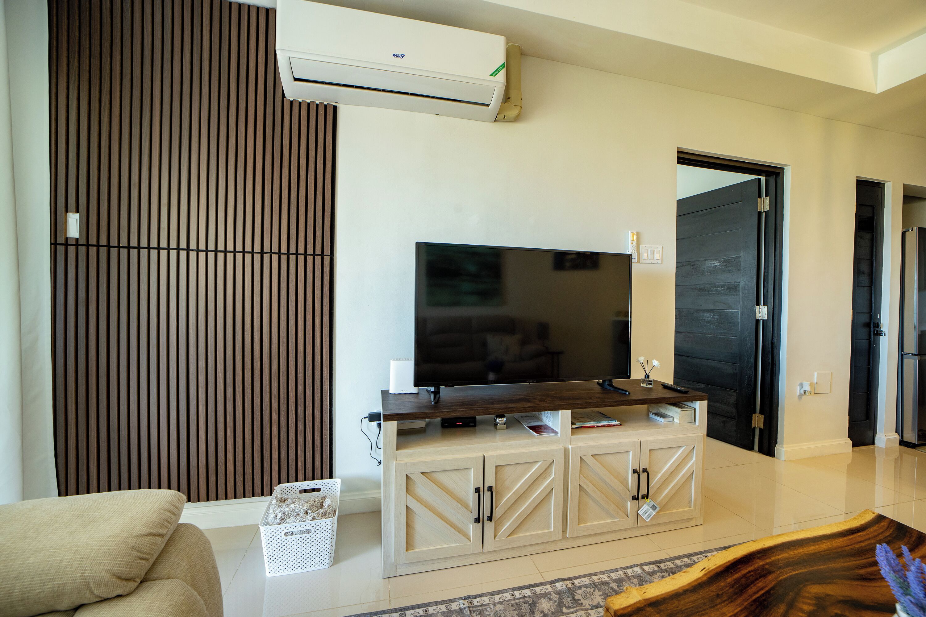 Una sala de estar moderna con un televisor de pantalla plana, un revestimiento de pared de madera y un mueble de entretenimiento de color claro.