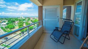 Un balcón con vista a un paisaje urbano, una puerta y dos sillas.