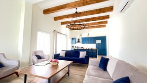 Una sala moderna con techo de madera, un juego de sofá, una mesa de centro y vista a la cocina.