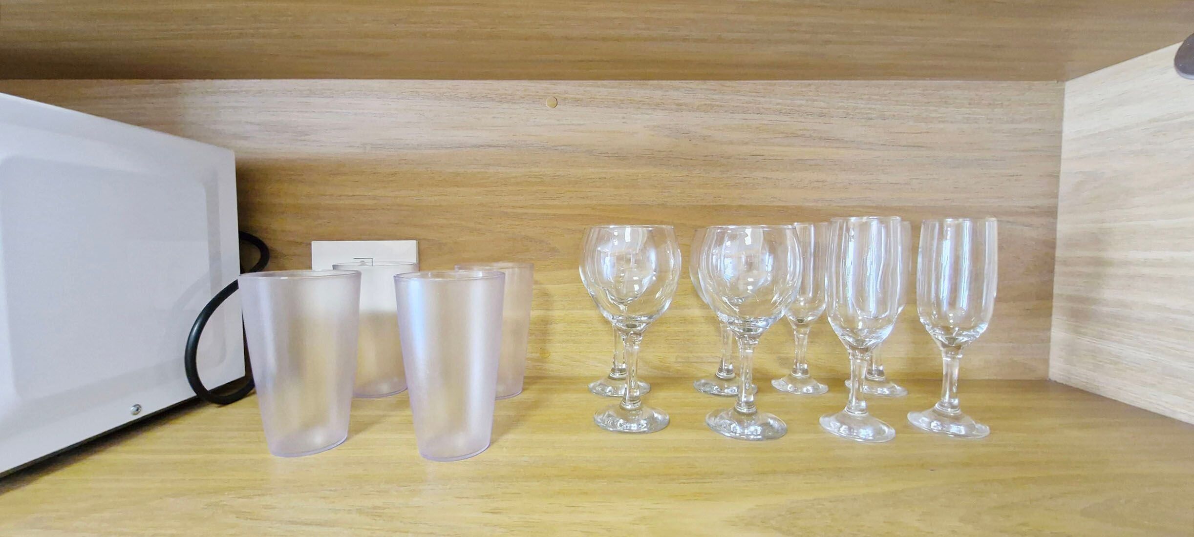 A wooden shelf with a white appliance and several clear glasses and tumblers.