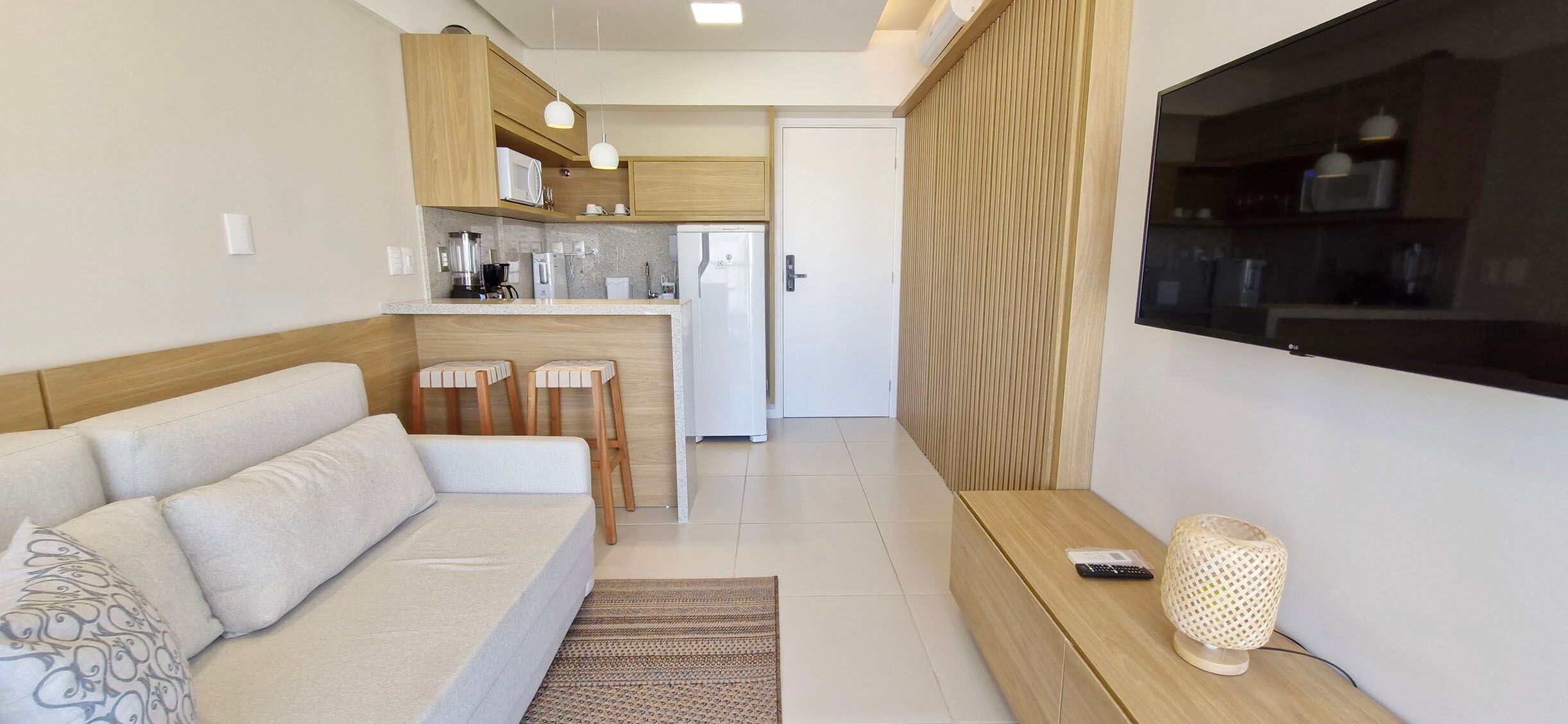 Un espacio habitable compacto con sofá, pequeña cocina y televisión montada en la pared.