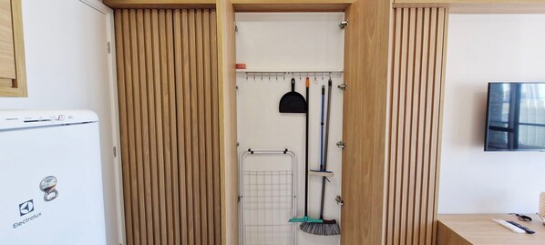 Una cocina compacta con refrigerador, armarios de madera y televisión montada en la pared.